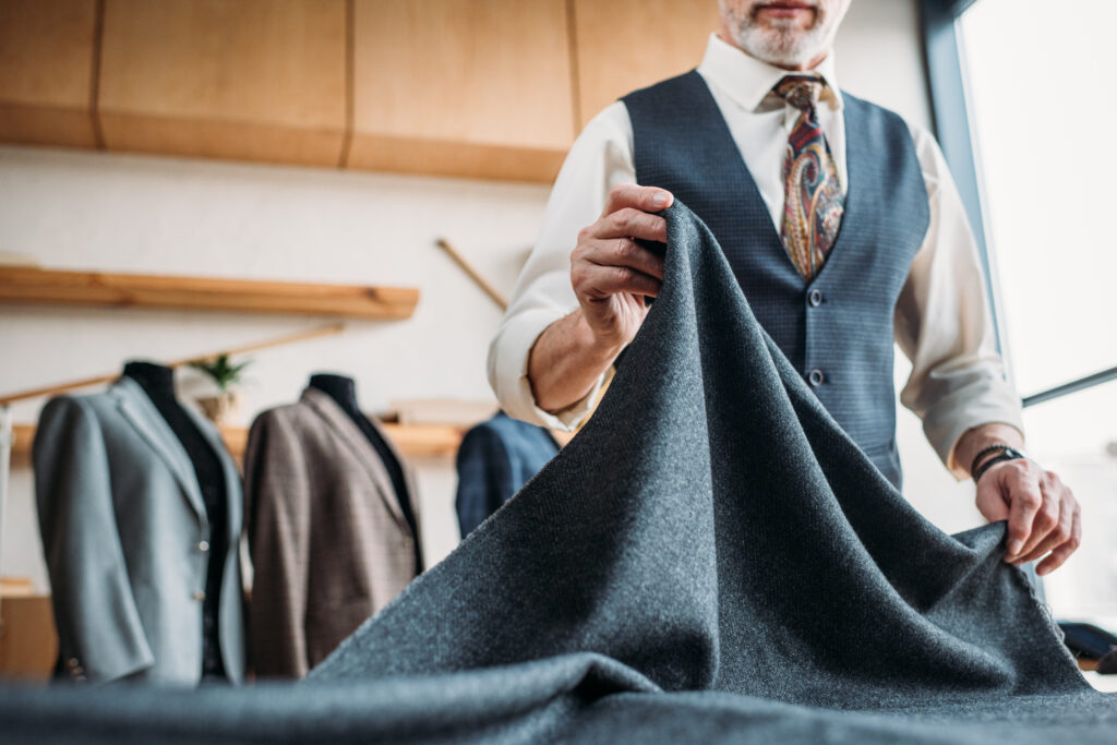 Cropped shot of stylish mature tailor with grey cloth at sewing workshop